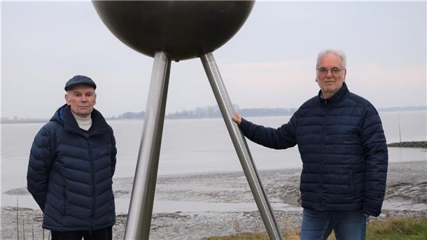 Zwei ältere Herren stehen neben dem Sonnen-Modell des Planetenwegs in Nordenham. 