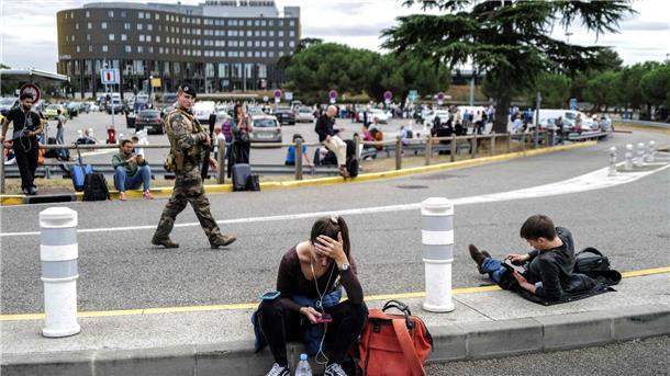 Reisende warten, während ein französischer Soldat vor dem Flughafen Toulouse-Blagnac patrouilliert.