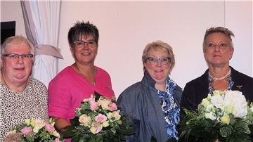 Vier Landfrauen stehen nebeneinander und halten Blumen in den Händen.
