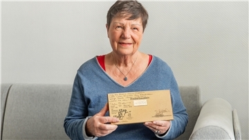 Eine Frau sitzt auf dem Sofa und hält einen rechteckigen beschriebenen Baustein in den Händen.