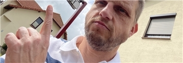 Reporter Bert Albers sitzt auf einer Mitfahrbank in Tarmstedt. Das Schild über ihm zeigt an, dass er ins Nachbardorf Wilstedt mitgenommen werden möchte.