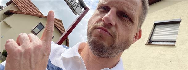 Reporter Bert Albers sitzt auf einer Mitfahrbank in Tarmstedt. Das Schild über ihm zeigt an, dass er ins Nachbardorf Wilstedt mitgenommen werden möchte.