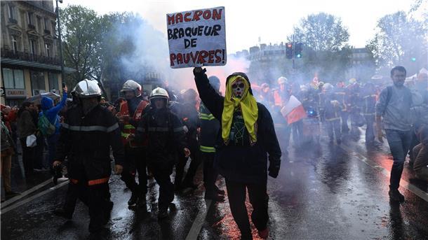 Rettungskräfte und ein Demonstrant mit einem Plakat mit der Aufschrift „Macron, Räuber der Armen“ marschieren während einer Demonstration anlässlich des Tages der Arbeit in Paris.