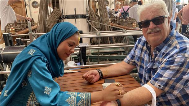 Richard Schwadorf lässt sich von Crew-Mitglied Hooa auf der Shabab Oman II mit Henna etwas auf den Arm schreiben