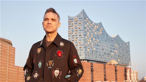 Robbie Williams auf einer Barkasse im Hamburger Hafen. Im Hintergrund ist die Elbphilharmonie zu sehen.