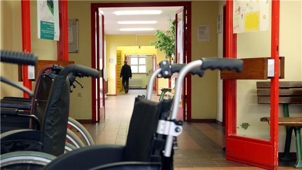 Rollstühle stehen vor einer Brandschutztür in einer Werkstatt für behinderte Menschen. Verbände kritisieren, dass diese besonders gefährdeten Menschen nicht früher gegen Corona geimpft werden.