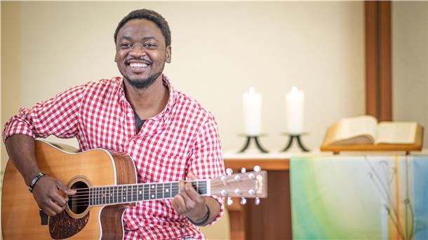 Ein Mann sitzt vor einem Altar und spielt Gitarre.