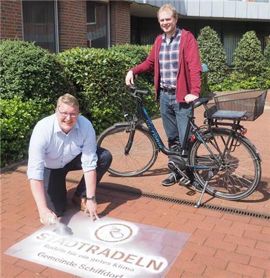 In Schiffdorf zählt jeder mit dem Fahrrad zurückgelegte Kilometer Schiffdorfs Bürgermeister Henrik Wärner sprüht per Schablone Kreide auf den Zugang zum Rathaus. Klimaschutzmanager Birger Auffahrt steht mit einem Fahrrad hinter ihm.