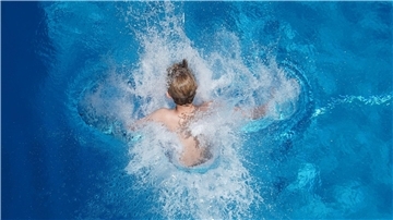 Ein Junge klatscht in einem Schwimmbad ins Wasser