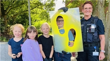 Vier Grundschulkinder mit einer Polizistin halten eine Schablone, aus der zwei Fußabdrücke ausgeschnitten sind.