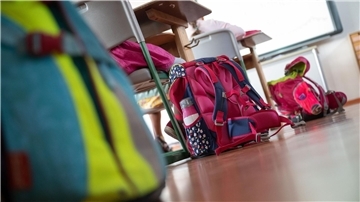 Schulranzen stehen in einem Klassenraum auf dem Boden.