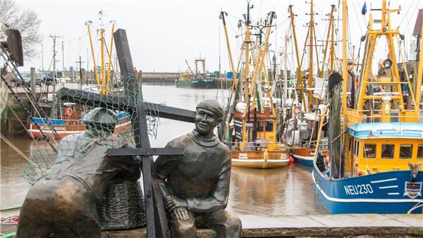Schwarze Holzkreuze lehnen an der Bronezeskulptur „Alt- und Jungfischer“ im Hafen in Neuharlingersiel. Das Fischen mit Grundschleppnetzen steht in der Kritik.
