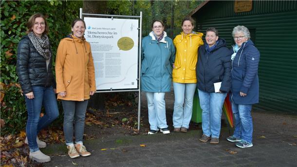 Sechs Frauen stehen links und rechts neben einer großen Tafel an einem Parkzugang.