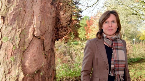 Eine Frau mit Schal steht neben einem Baum.