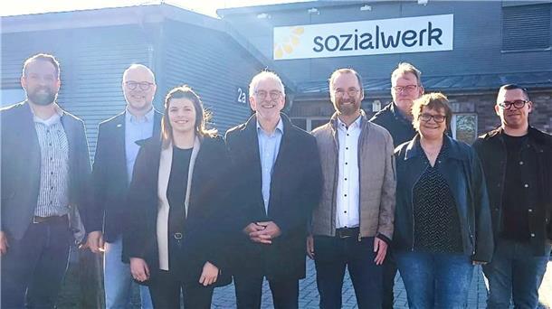 Acht Menschen stehen vor einer großen Halle mit der Aufschrift "sozialwerk". 