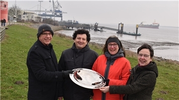 Vier Pastoren stehen in Nordenham am Weserstrand und werben für ein Tauffest im Juni.
