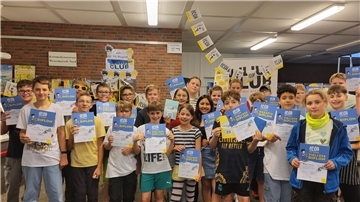 Über 20 Kinder stehen zusammen und halten lächelnd Diplome in den Händen. 