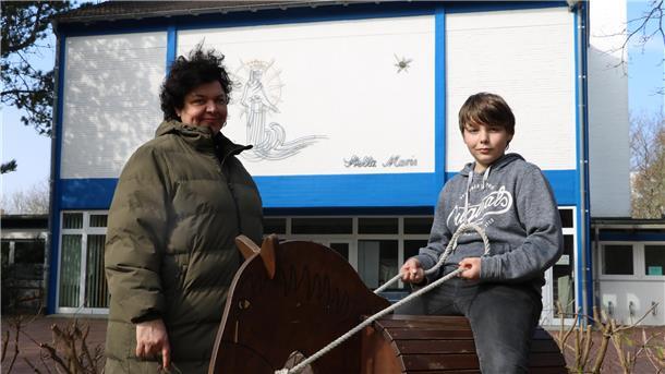 Eine Mutter steht mit ihrem Sohn vor einem Gebäude. 