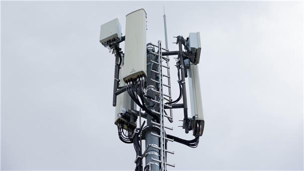 Im Vordergrund ist ein Mobilfunkmast zu sehen, dahinter ein wolkenverhangener grauer Himmel.