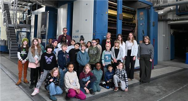 Viele Schülerinnen und Schüler stehen mit Lehrern vor einer großen Druckmaschine.