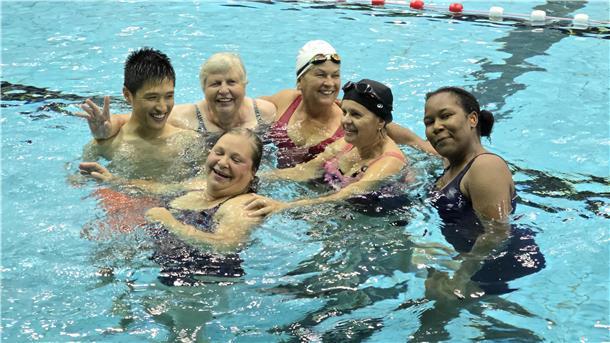 sechs gut gelaunte Personen in Badebekleidung in einem Schwimmbecken