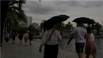Spaziergänger mit Regenschirmen sind an der Strandpromenade von Palma unterwegs.