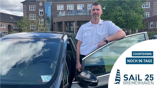 Mann lehnt an einer Autotür: Stabsbootsmann Eik Schomann organisiert den Fahrdienst für Kapitäne, Crew und Ehrengäste während der Sail in Bremerhaven.