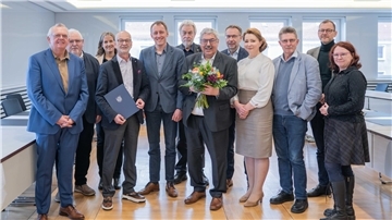 Ein Gruppenfoto mit mehreren Mitarbeitern der Stadt Bremerhaven. Der Vierte von links hält eine Urkunde in seiner Hand, ein Mann in der Mitte einen Blumenstrauß. Es geht um die Verabschiedung eines Stadtrats.