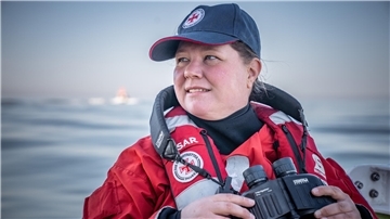 Seenotretterin Stefanie Riemer hält ein Fernglas in der Hand. Sie ist an Board eines Seenotrettungsbootes der deutschen Gesellschaft zur Rettung Schiffbrüchiger.