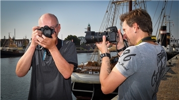Männer mit Fotokameras vor einem Schiff.