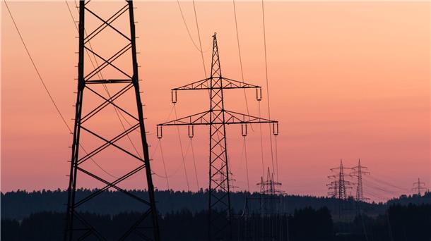 Länder fordern Brückenstrompreis für Industrie Strommasten sind bei Sonnenaufgang als Silhouette zu sehen.