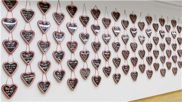 Zahlreiche Lebkuchenherzen mit Sprüchen hängen an einer Wand. 