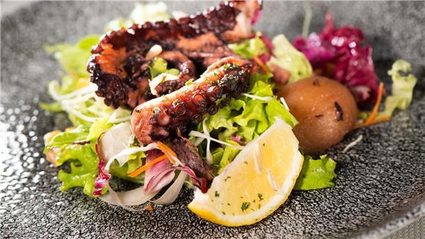 Gegrillter Oktopus liegt auf einer Salatbeilage auf einem Teller.