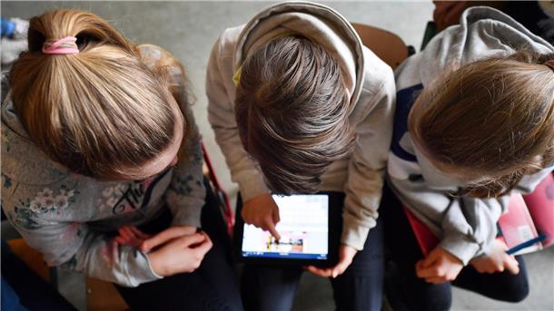 Drei Kinder schauen auf ein Tablet.