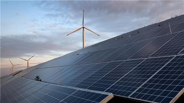 Im Vordergrund sind Photovoltaikanlagen zu sehen, im Hintergrund Windenergieanlagen.