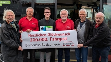 Sechs Männer mit einem Banner. Der Bürger Butjadingen hat den 200.000. Fahrgast begrüßt. 