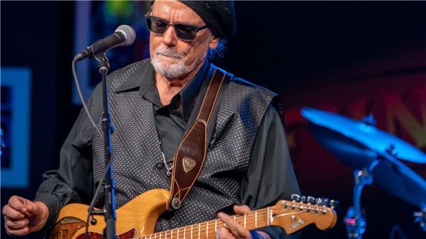 Ein Mann am Mikrofon mit einer Gitarre. Blues-Musiker Tas Cru spielt in der Jahnhalle. 