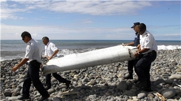 Techniker tragen ein Wrackteil, die Flügelklappe eines Flugzeugs, über einen Strand bei Saint-André,  Réunion.