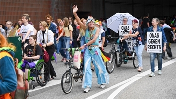 Eine Gruppe von Menschen, die am Christopher-Street-Day teilgenommen haben. In der Mitte ist eine ältere Frau mit Deutschlandfahne und einem Fahrrad, dahinter eine Frau mit einem Plakat und der Botschaft: Omas gegen rechts.   