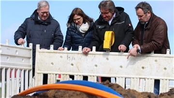 Die Vier stehen vor einer Baustellenabsperrung und schauen hinunter auf ein Glasfaserkabel.