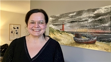 Eine Frau steht lächelnd vor einem maritimen Wandbild.