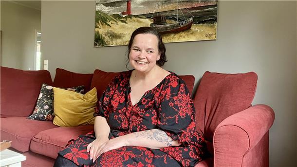 Eine lächelnde übergewichtige Frau sitzt auf einem roten Sofa. 