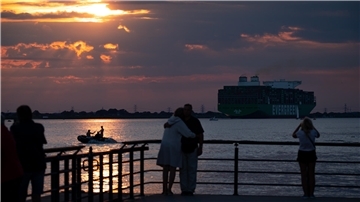 Touristen beobachten den Sonnenuntergang, während ein Containerschiff vorbeifährt. Um Künstliche Intelligenz im Tourismus geht beim NordseeTourismusTag 2024 in Bremerhaven. 