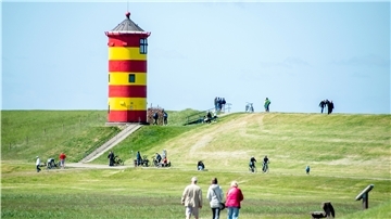 Touristen gehen auf dem Deich vor dem Pilsumer Leuchtturm in der Gemeinde Krummhörn spazieren.