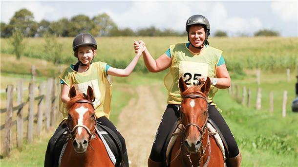 Die Distanzreiterinnen: Ariane und Tuana Ebsen aus Tossens Ein Mädchen und eine Frau sitzen jeweils auf einem braunen Pferd. Sie reiten nebeneinander und halten sich triumphierend die Hände.