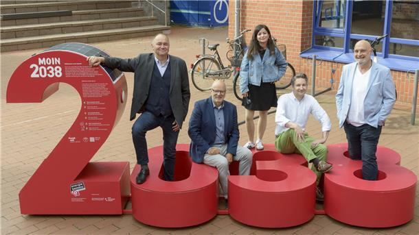 Fünf Personen stehen und sitzen um die rote Installation „MOIN 2038“ auf dem Campus der Hochschule Bremerhaven, die symbolisch für das Klimaziel des Landes Bremen steht.