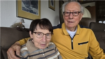 Eine ältere Frau und ein älterer Mann schauen in die Kamera, der Mann hat den Arm um die Schulter der Frau gelegt.