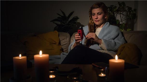 Eine Frau hält bei einem Stromausfall eine Taschenlampe in der Hand, bei der mit Hilfe einer Kurbel Energie erzeugt werden kann.