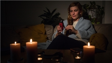 Eine Frau hält bei einem Stromausfall eine Taschenlampe in der Hand, bei der mit Hilfe einer Kurbel Energie erzeugt werden kann.
