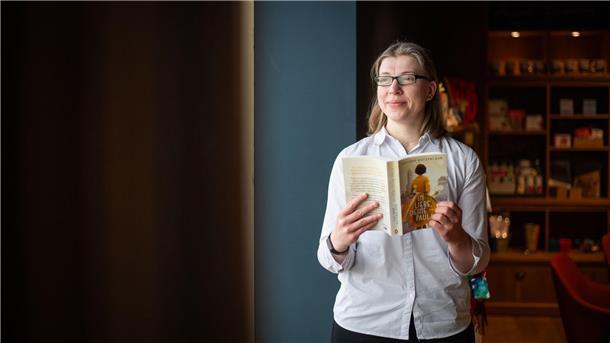 Eine Frau mit weißer Bluse trägt hält ein Buch in der Hand.